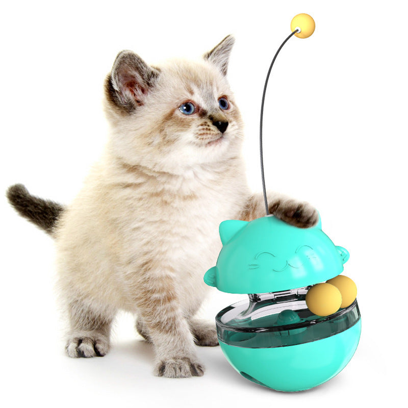 A fluffy cream-colored kitten with dark ears and paws is interacting with a turquoise cat toy that has a long black antenna and yellow balls inside, photographed on a clean white background.